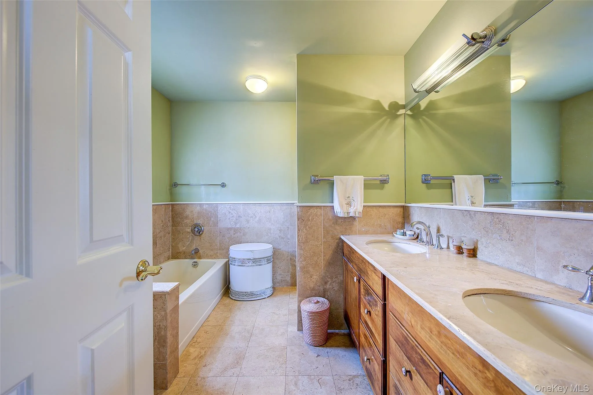 Full bath with tile walls, double vanity, a garden tub, a wainscoted wall, and light tile patterned flooring Full bath with tile walls, double vanity, a garden tub, a wainscoted wall, and light tile patterned flooring
