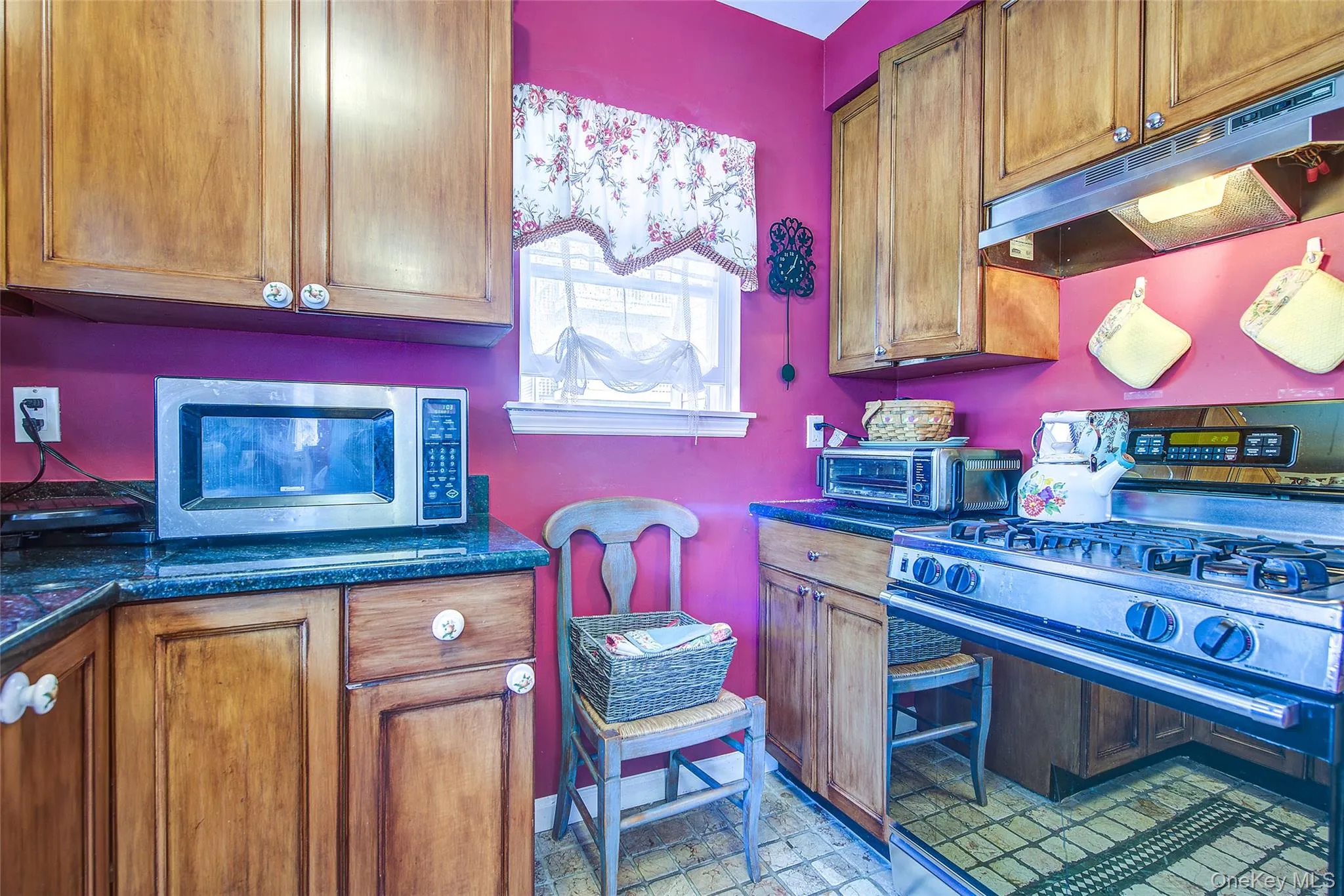 Kitchen featuring appliances with stainless steel finishes, dark countertops, brown cabinets, and under cabinet range hood Kitchen featuring appliances with stainless steel finishes, dark countertops, brown cabinets, and under cabinet range hood