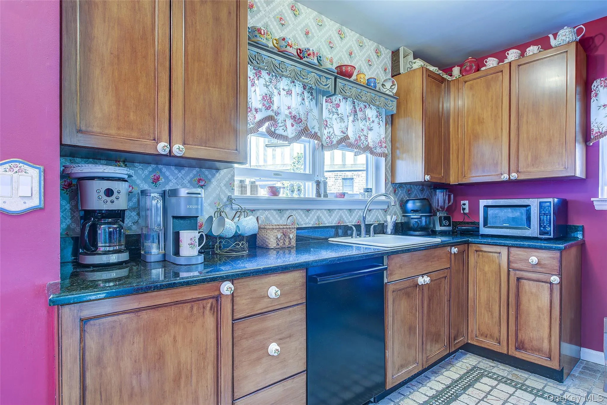 Kitchen with black dishwasher, tasteful backsplash, stainless steel microwave, and brown cabinets Kitchen with black dishwasher, tasteful backsplash, stainless steel microwave, and brown cabinets