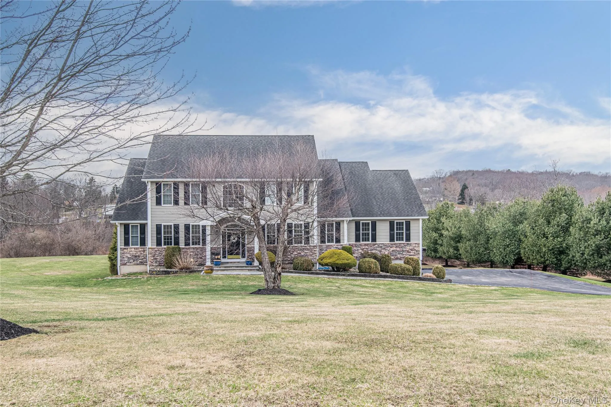 Colonial inspired home featuring stone siding and a front yard Colonial inspired home featuring stone siding and a front yard