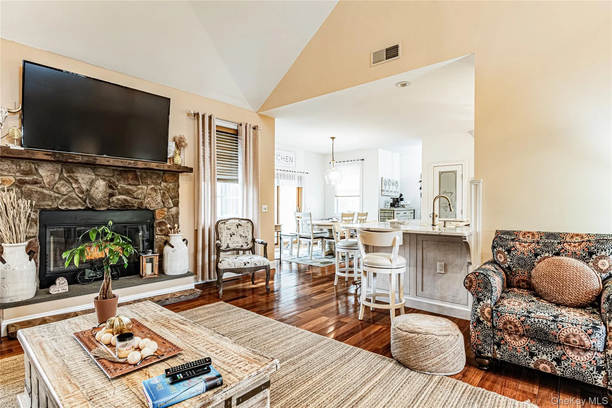 Living area with vaulted ceiling, wood-style flooring, and a stone fireplace Living area with vaulted ceiling, wood-style flooring, and a stone fireplace