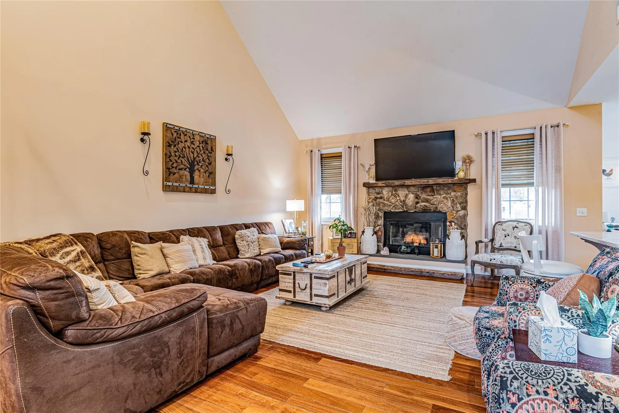 Living room featuring wood-type flooring, lofted ceiling, healthy amount of natural light, and a stone fireplace Living room featuring wood-type flooring, lofted ceiling, healthy amount of natural light, and a stone fireplace