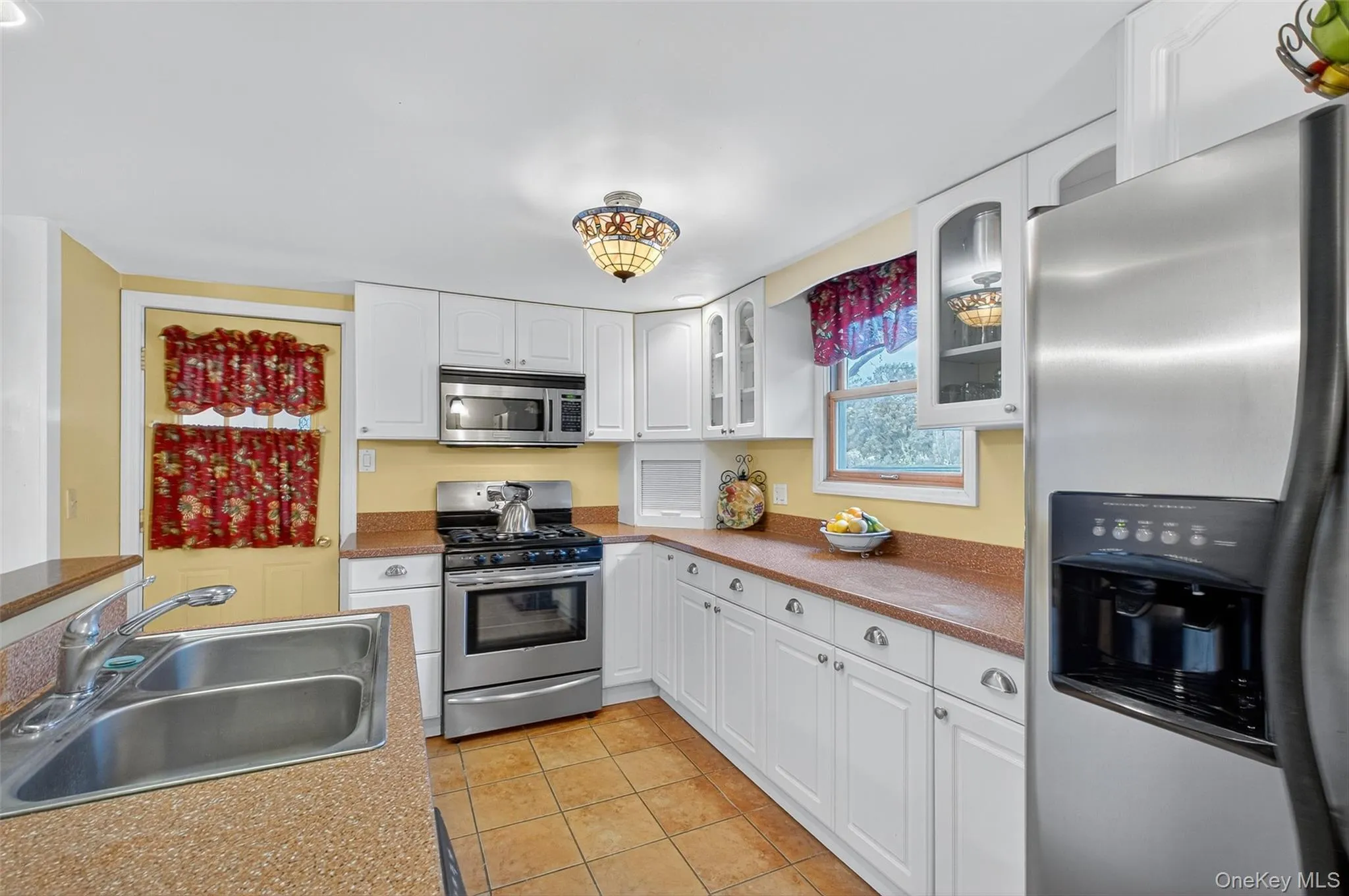 Kitchen with stainless steel appliances, white cabinets, glass insert cabinets, light tile patterned floors, and light countertops Kitchen with stainless steel appliances, white cabinets, glass insert cabinets, light tile patterned floors, and light countertops