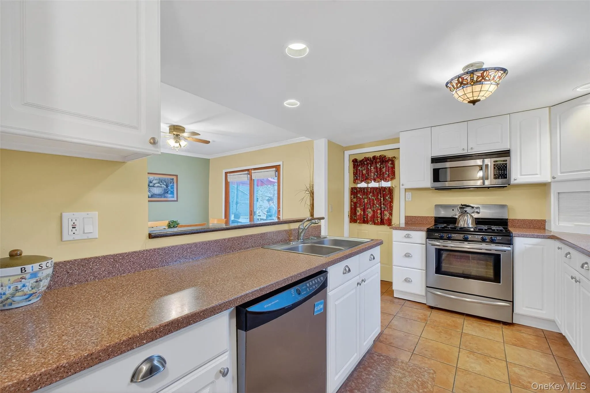 Kitchen with stainless steel appliances, white cabinetry, light tile patterned floors, recessed lighting, and ornamental molding Kitchen with stainless steel appliances, white cabinetry, light tile patterned floors, recessed lighting, and ornamental molding
