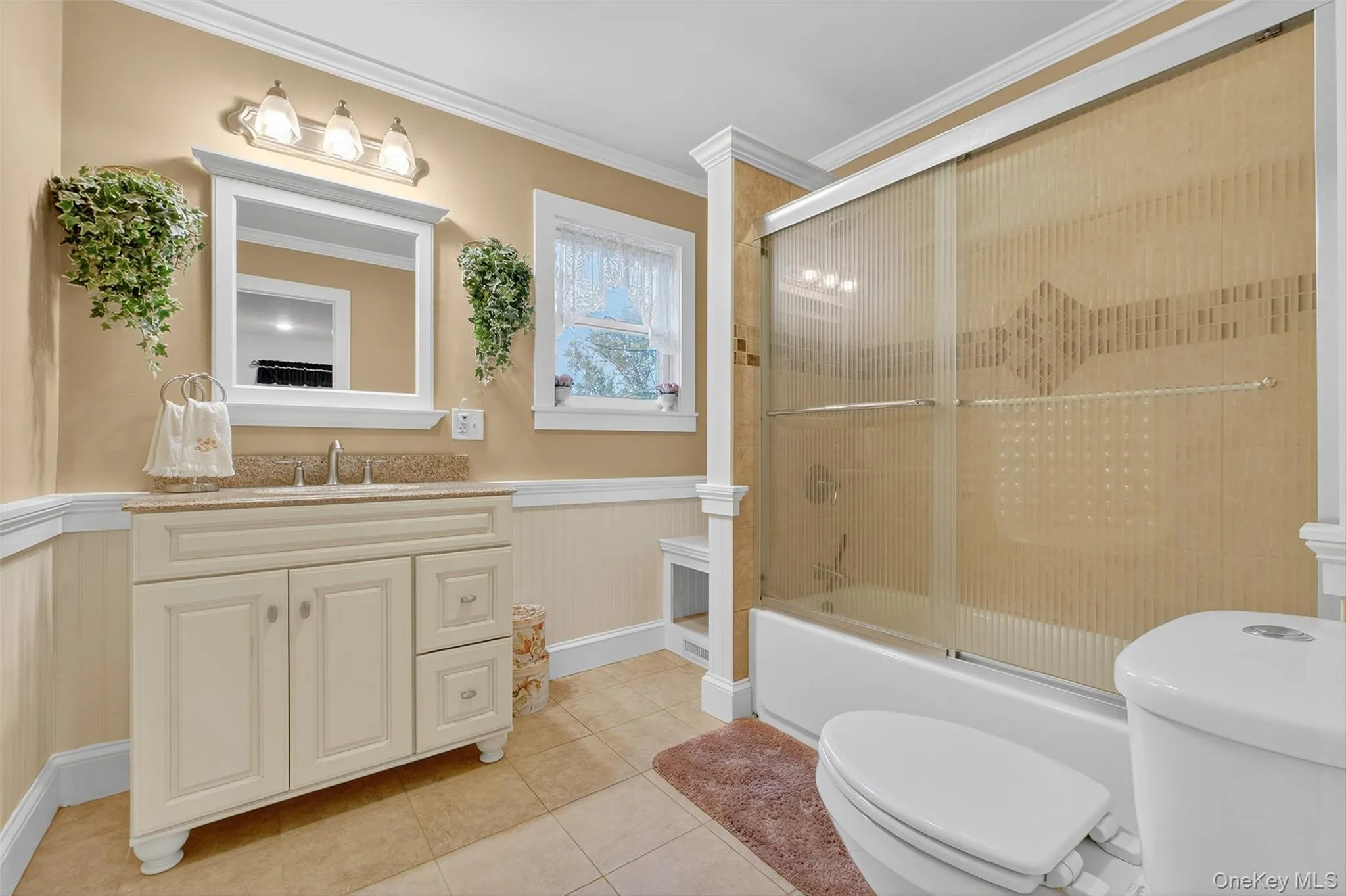 Full bathroom with a wainscoted wall, crown molding, enclosed tub / shower combo, light tile patterned floors, and vanity Full bathroom with a wainscoted wall, crown molding, enclosed tub / shower combo, light tile patterned floors, and vanity