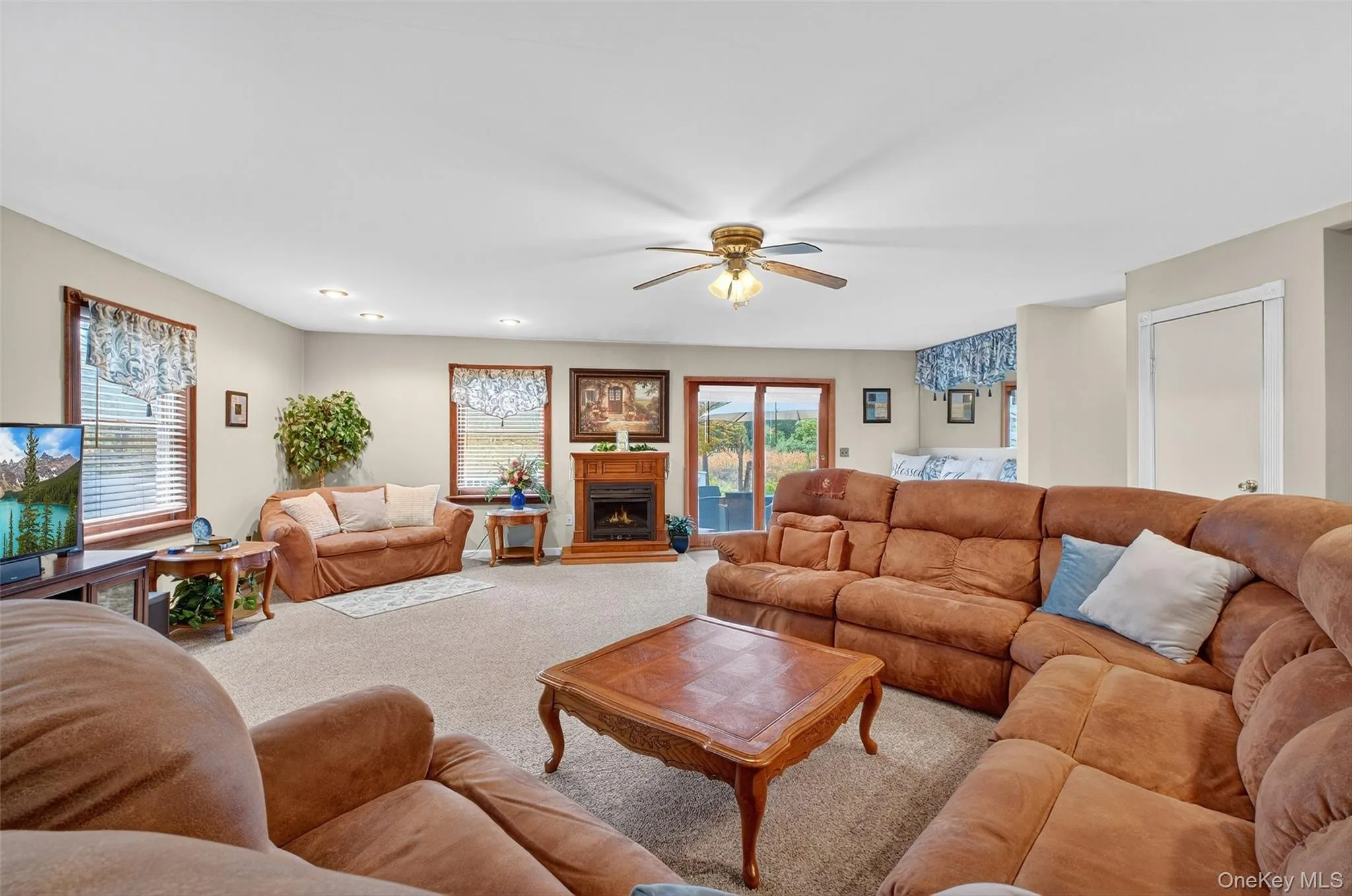 Living area featuring carpet flooring, a ceiling fan, and a lit fireplace Living area featuring carpet flooring, a ceiling fan, and a lit fireplace