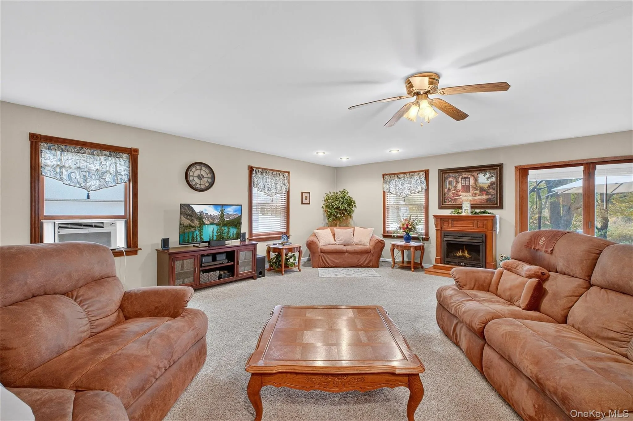 Living area featuring a lit fireplace, carpet, a ceiling fan, and cooling unit Living area featuring a lit fireplace, carpet, a ceiling fan, and cooling unit