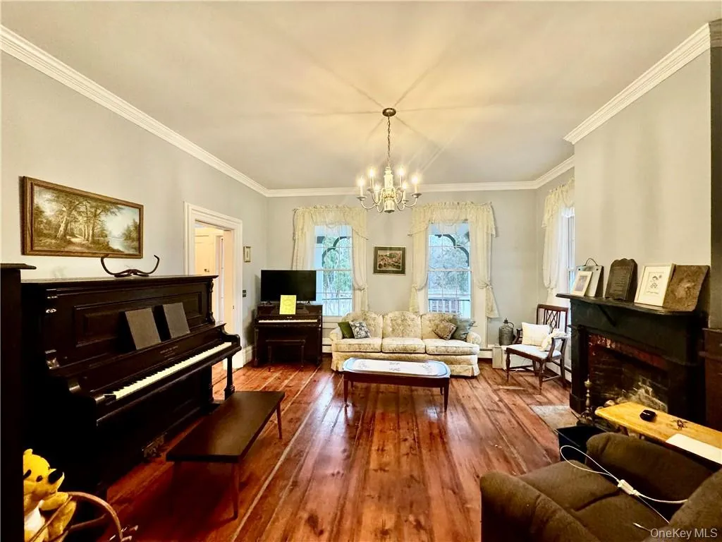 Living room featuring crown molding, a notable chandelier, and wood-type flooring Living room featuring crown molding, a notable chandelier, and wood-type flooring