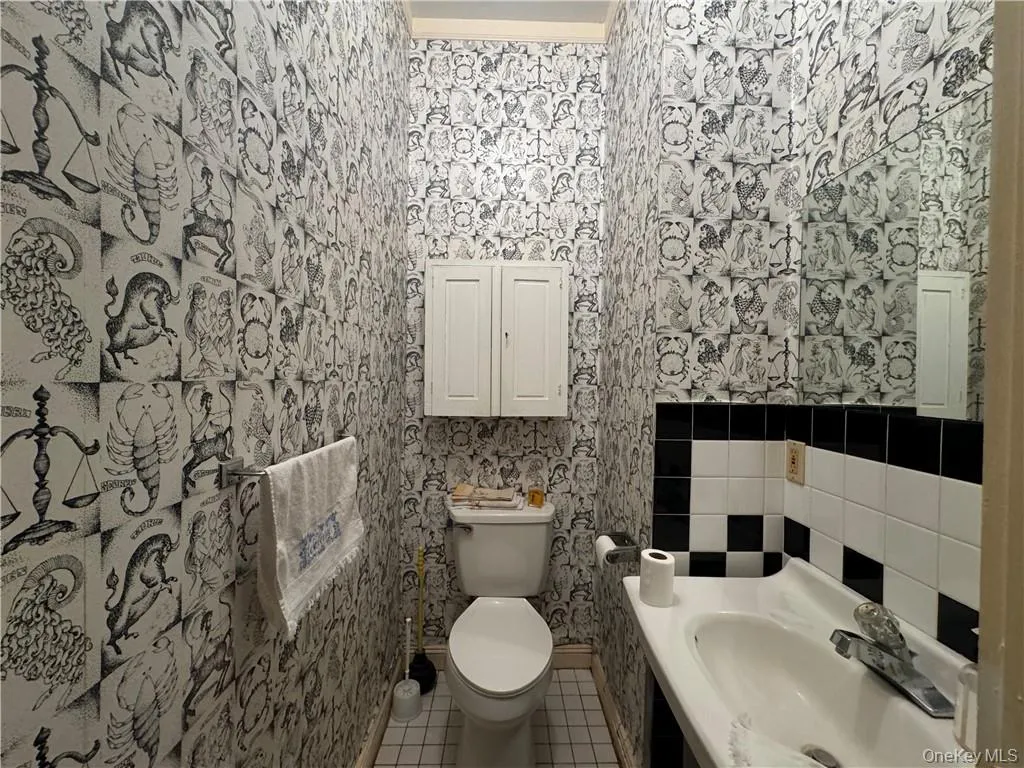 1st floor Bathroom featuring toilet, tile patterned flooring, ornamental molding, sink, and tile walls 1st floor Bathroom featuring toilet, tile patterned flooring, ornamental molding, sink, and tile walls