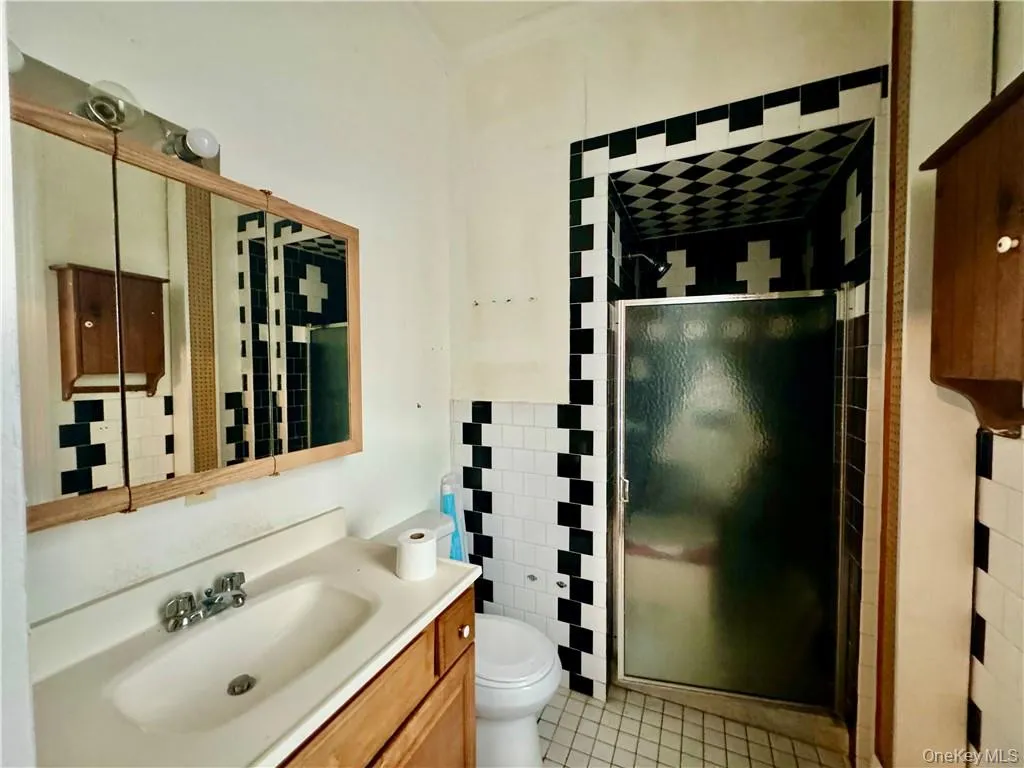 Bathroom featuring a shower with shower door, toilet, tile patterned floors, tile walls, and vanity Bathroom featuring a shower with shower door, toilet, tile patterned floors, tile walls, and vanity