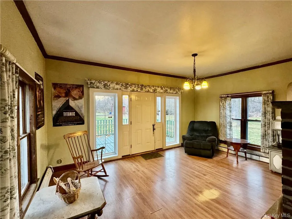 Sitting room with baseboard heating, ornamental molding, a notable chandelier, and wood-type flooring Sitting room with baseboard heating, ornamental molding, a notable chandelier, and wood-type flooring