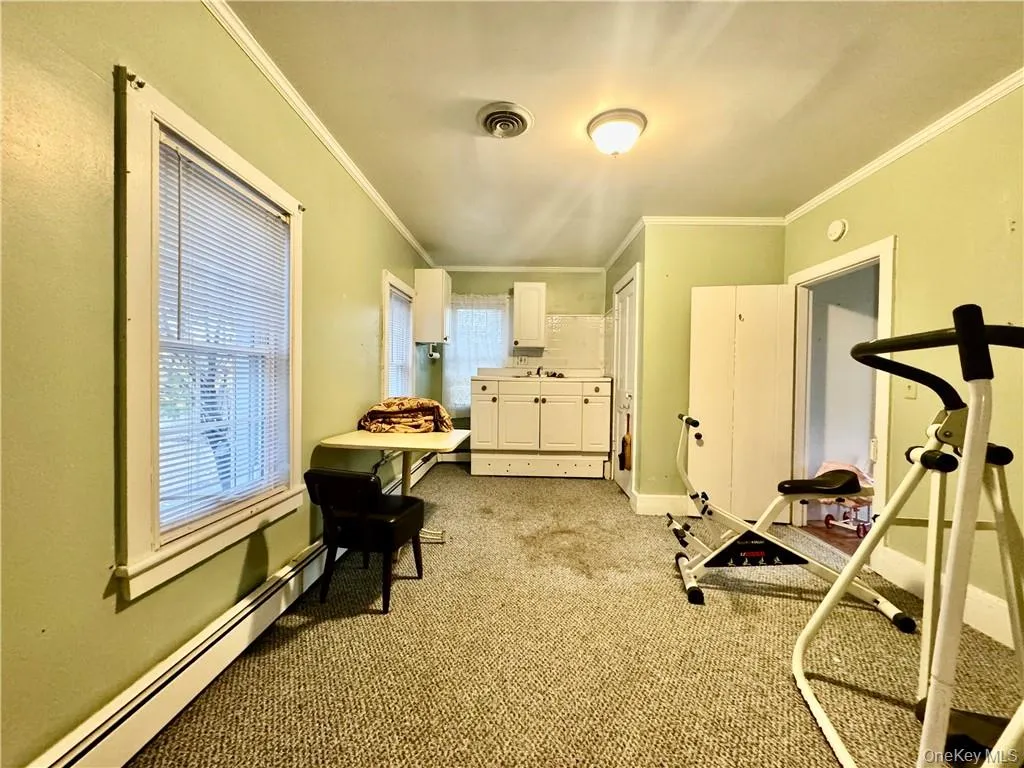 Workout area featuring ornamental molding, light carpet, and a baseboard radiator Workout area featuring ornamental molding, light carpet, and a baseboard radiator