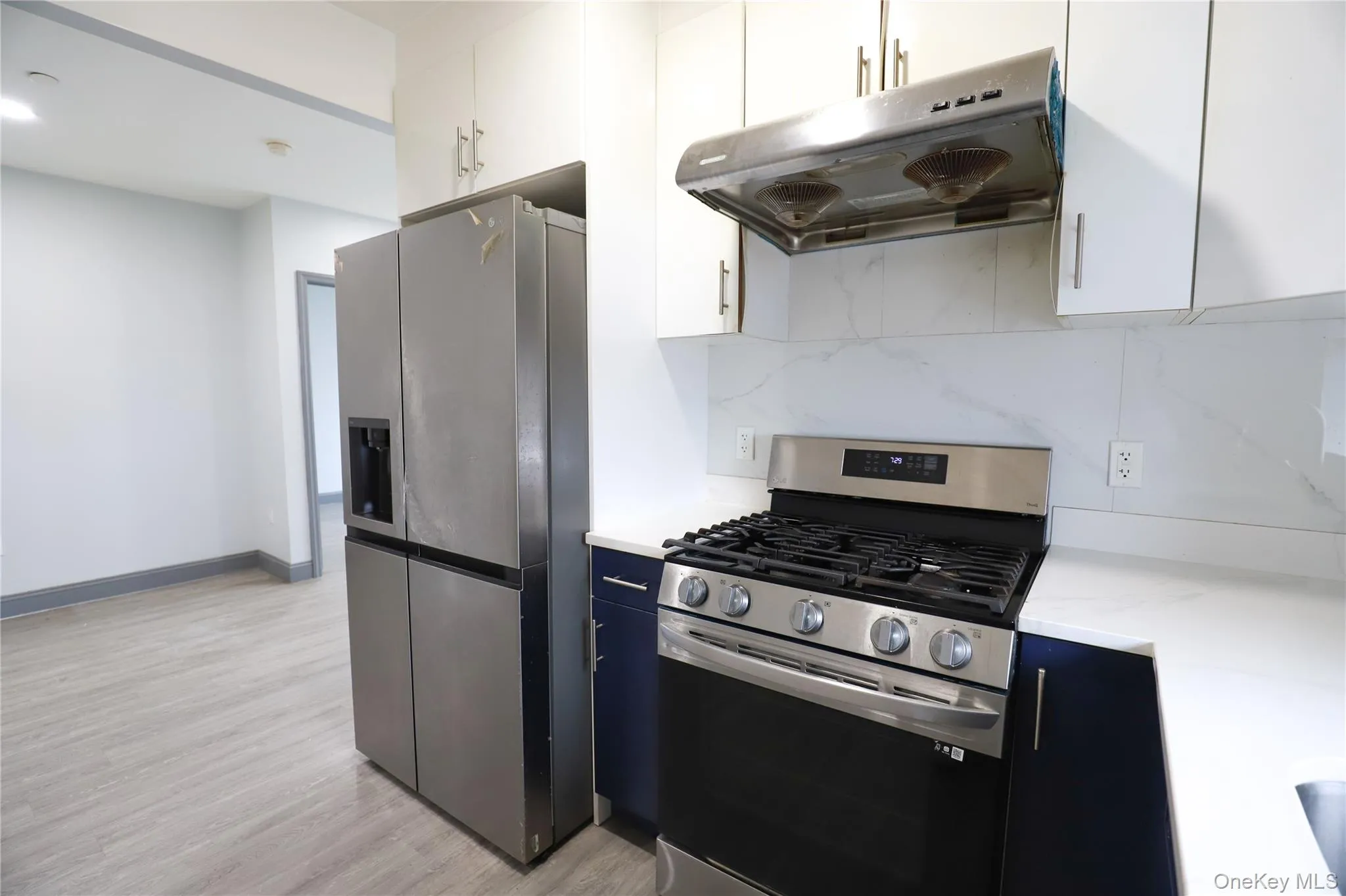 Kitchen featuring stainless steel appliances, light wood-style floors, decorative backsplash, dual tone cabinetry, and light stone counters Kitchen featuring stainless steel appliances, light wood-style floors, decorative backsplash, dual tone cabinetry, and light stone counters