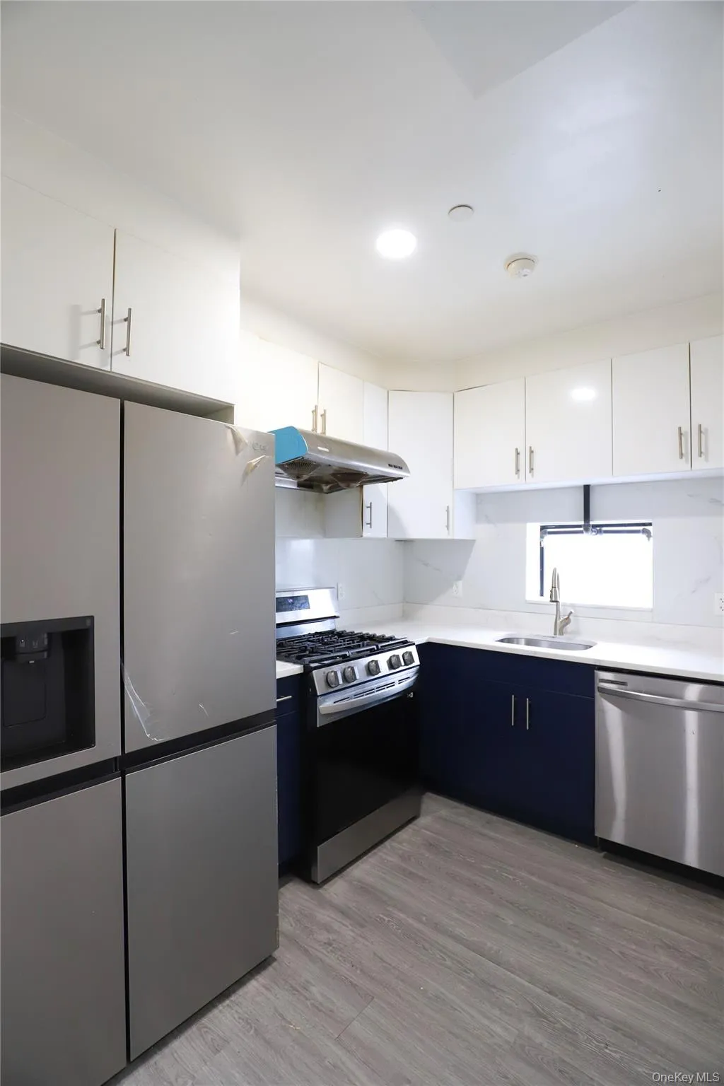 Dual tone kitchen featuring stainless steel appliances, dual tone cabinets, light countertops, and light wood-style flooring Dual tone kitchen featuring stainless steel appliances, dual tone cabinets, light countertops, and light wood-style flooring