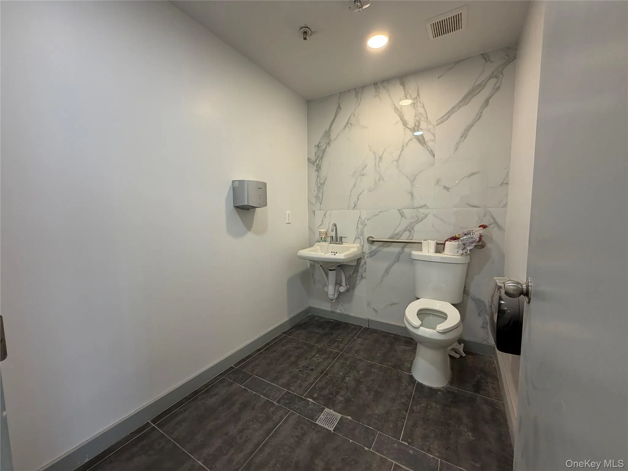 Bathroom with recessed lighting, dark tile patterned floors, and stone wall Bathroom with recessed lighting, dark tile patterned floors, and stone wall