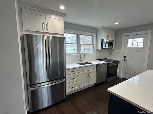 Kitchen with stainless steel appliances, white cabinets, dark wood-style flooring, recessed lighting, and light stone countertops Kitchen with stainless steel appliances, white cabinets, dark wood-style flooring, recessed lighting, and light stone countertops