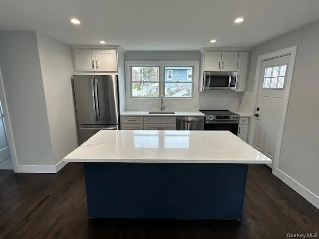 Two tone kitchen featuring stainless steel appliances, a center island, dark wood-style flooring, light stone countertops, and recessed lighting Two tone kitchen featuring stainless steel appliances, a center island, dark wood-style flooring, light stone countertops, and recessed lighting