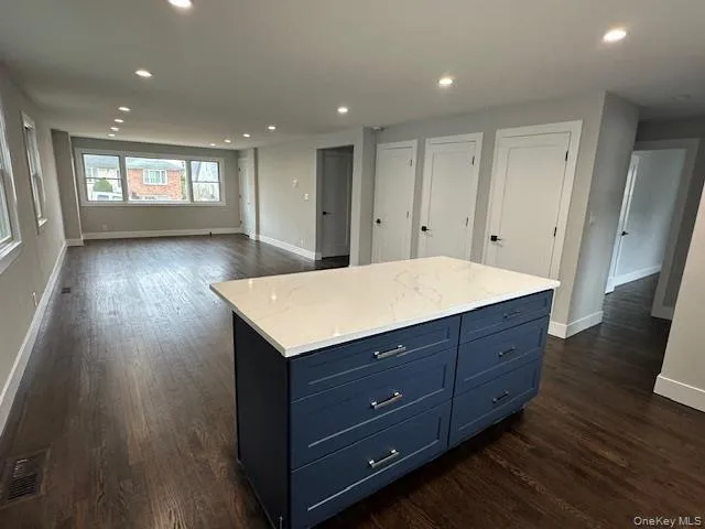 Kitchen with a kitchen island, blue cabinets, light stone countertops, recessed lighting, and dark wood-style flooring Kitchen with a kitchen island, blue cabinets, light stone countertops, recessed lighting, and dark wood-style flooring