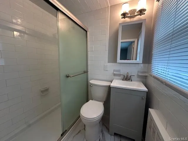 Bathroom featuring vanity, a shower stall, tile walls, and light marble finish flooring Bathroom featuring vanity, a shower stall, tile walls, and light marble finish flooring