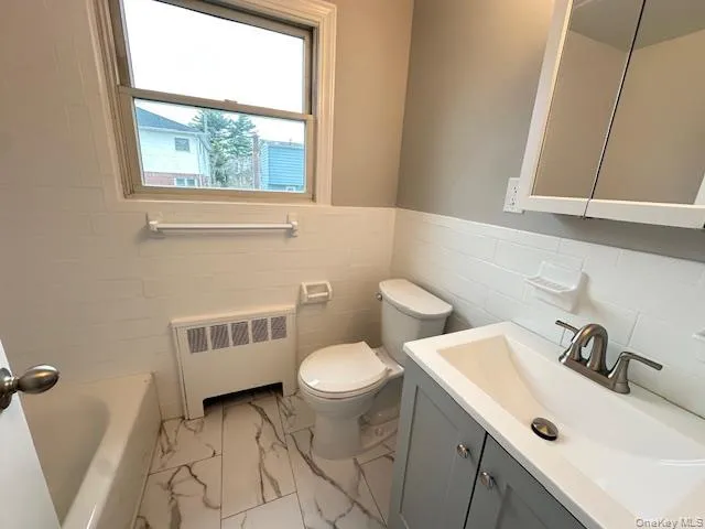 Bathroom with vanity, radiator, a tub to relax in, a wainscoted wall, and tile walls Bathroom with vanity, radiator, a tub to relax in, a wainscoted wall, and tile walls