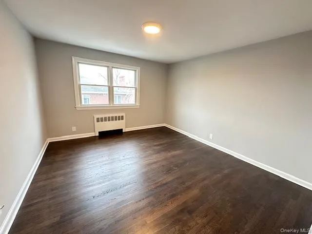 Bedroom featuring dark wood-type flooring and radiator heating unit Bedroom featuring dark wood-type flooring and radiator heating unit