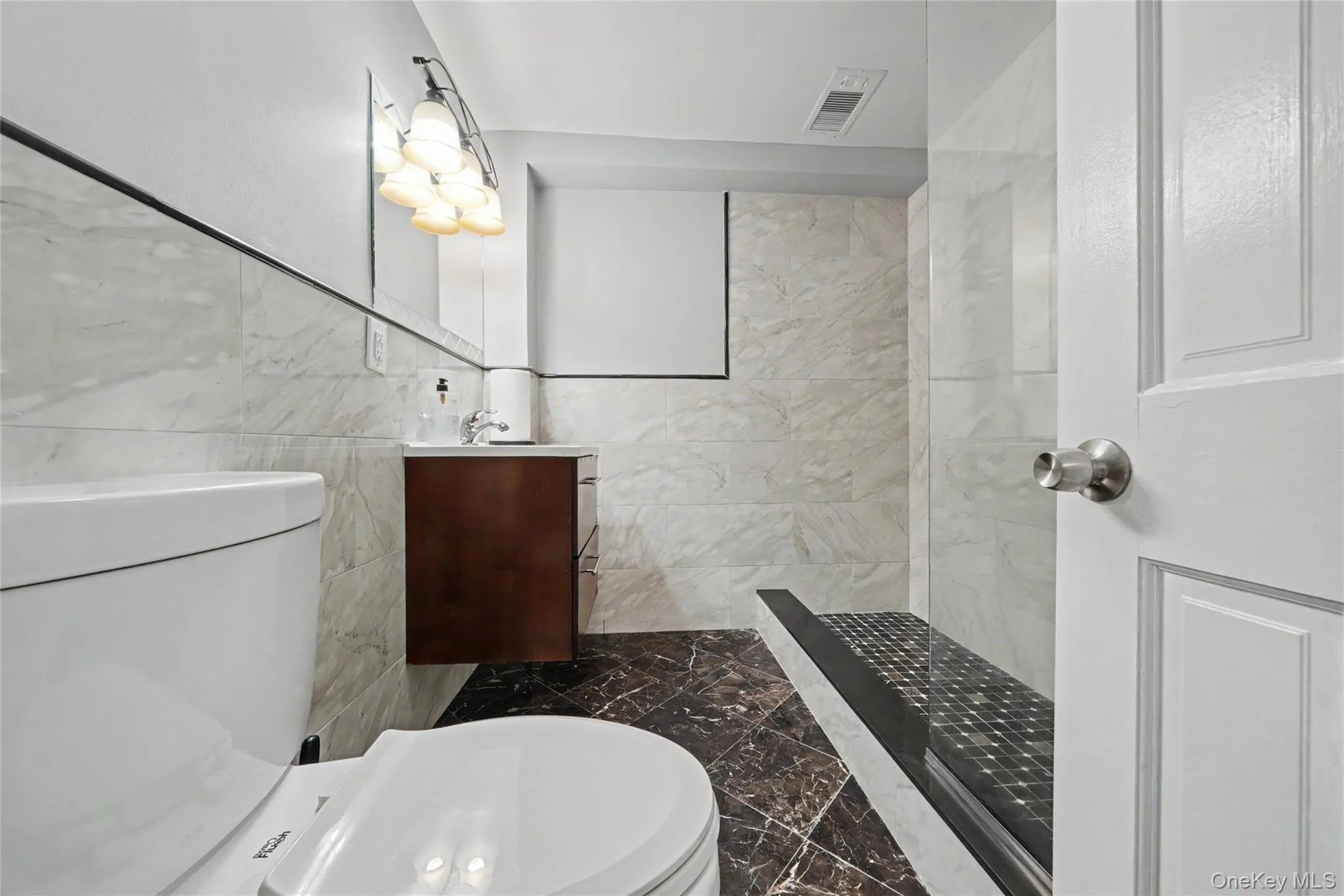 Full bathroom with vanity, tile walls, dark marble finish flooring, and a walk in shower Full bathroom with vanity, tile walls, dark marble finish flooring, and a walk in shower