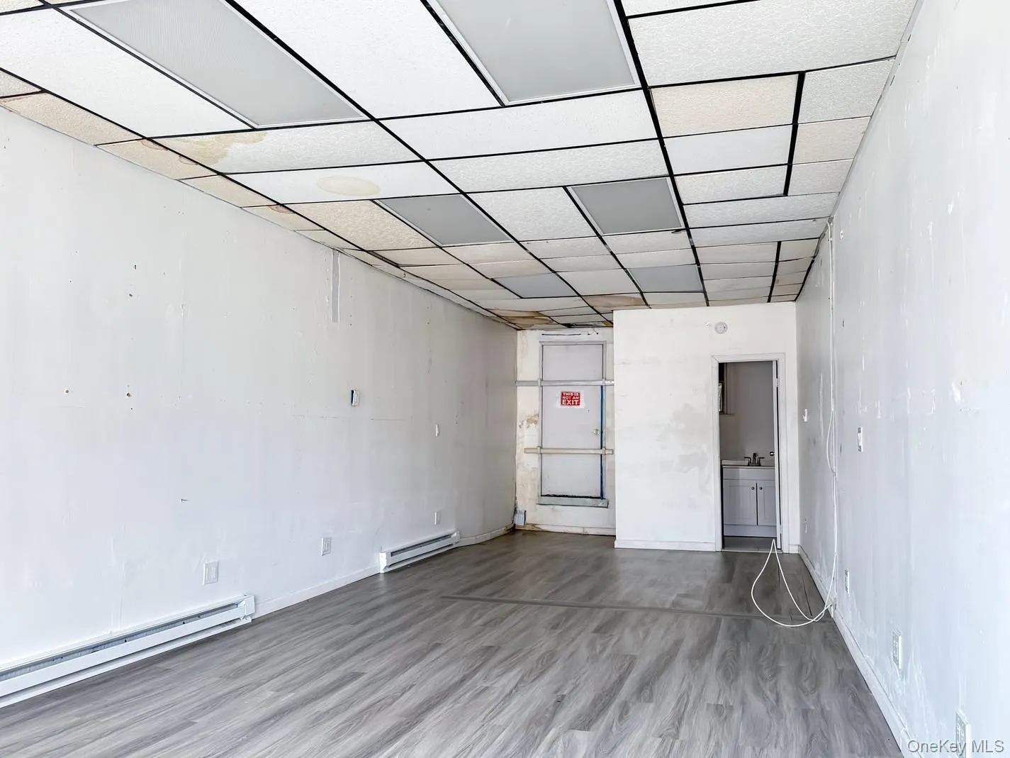 Empty commercial space featuring a paneled ceiling, a baseboard heating unit, and wood finished floors Empty commercial space featuring a paneled ceiling, a baseboard heating unit, and wood finished floors