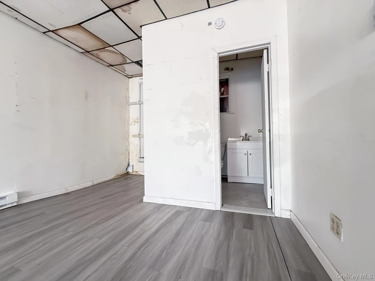 Empty commercial space with a paneled ceiling and dark wood-style flooring with Bathroom door Empty commercial space with a paneled ceiling and dark wood-style flooring with Bathroom door
