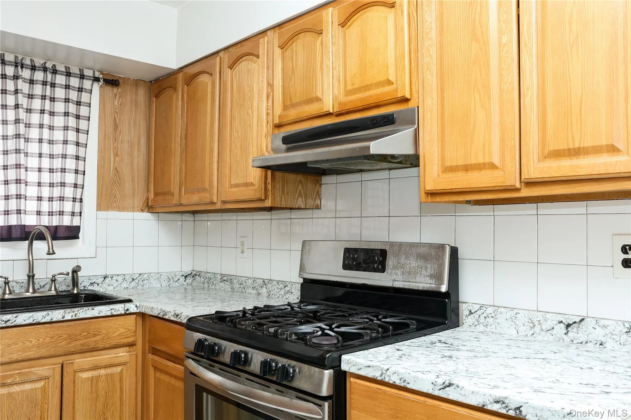 Kitchen featuring stainless steel range with gas stovetop, backsplash, wood finish cabinets, and light stone counters Kitchen featuring stainless steel range with gas stovetop, backsplash, wood finish cabinets, and light stone counters