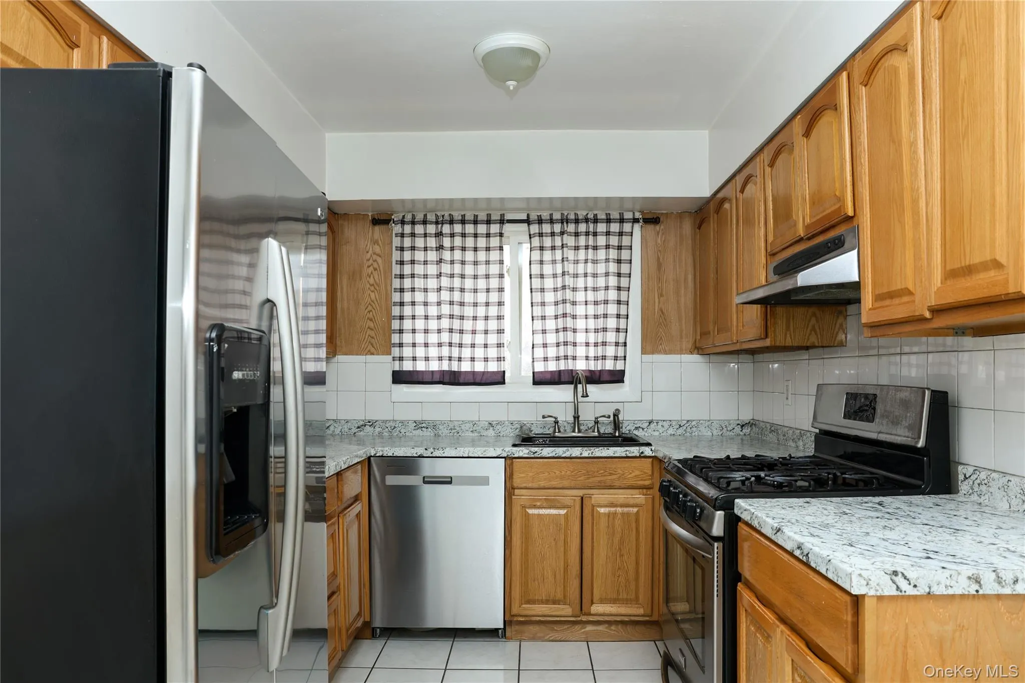 Kitchen with stainless steel appliances, wood finish cabinets, light tile patterned flooring, and tasteful backsplash Kitchen with stainless steel appliances, wood finish cabinets, light tile patterned flooring, and tasteful backsplash