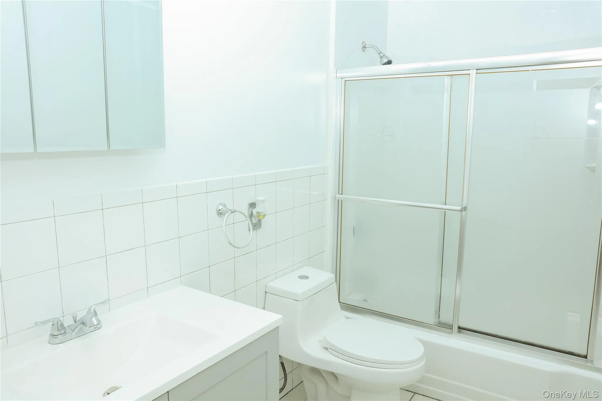 Bathroom featuring vanity, tile walls, enclosed tub / shower combo, and wainscoting Bathroom featuring vanity, tile walls, enclosed tub / shower combo, and wainscoting