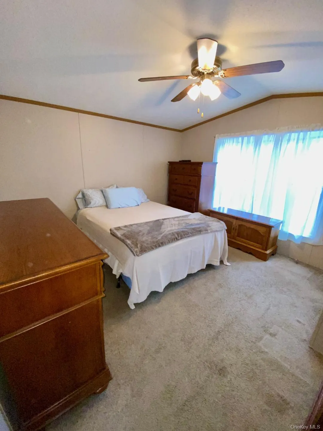 There's a spacious bedroom with a vaulted ceiling, light neutral carpet, crown molding, and a ceiling light fan. There's a spacious bedroom with a vaulted ceiling, light neutral carpet, crown molding, and a ceiling light fan.