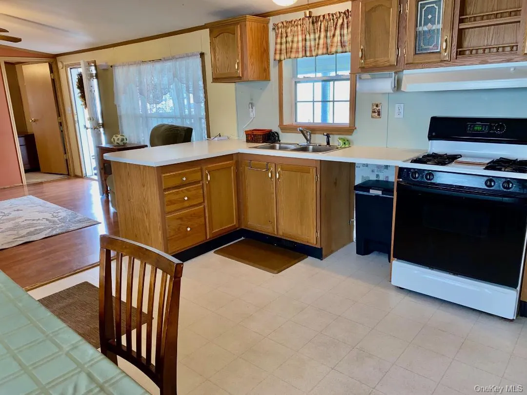 Kitchen featuring gas range oven, light countertops, a peninsula, wood finish cabinets, and crown molding Kitchen featuring gas range oven, light countertops, a peninsula, wood finish cabinets, and crown molding