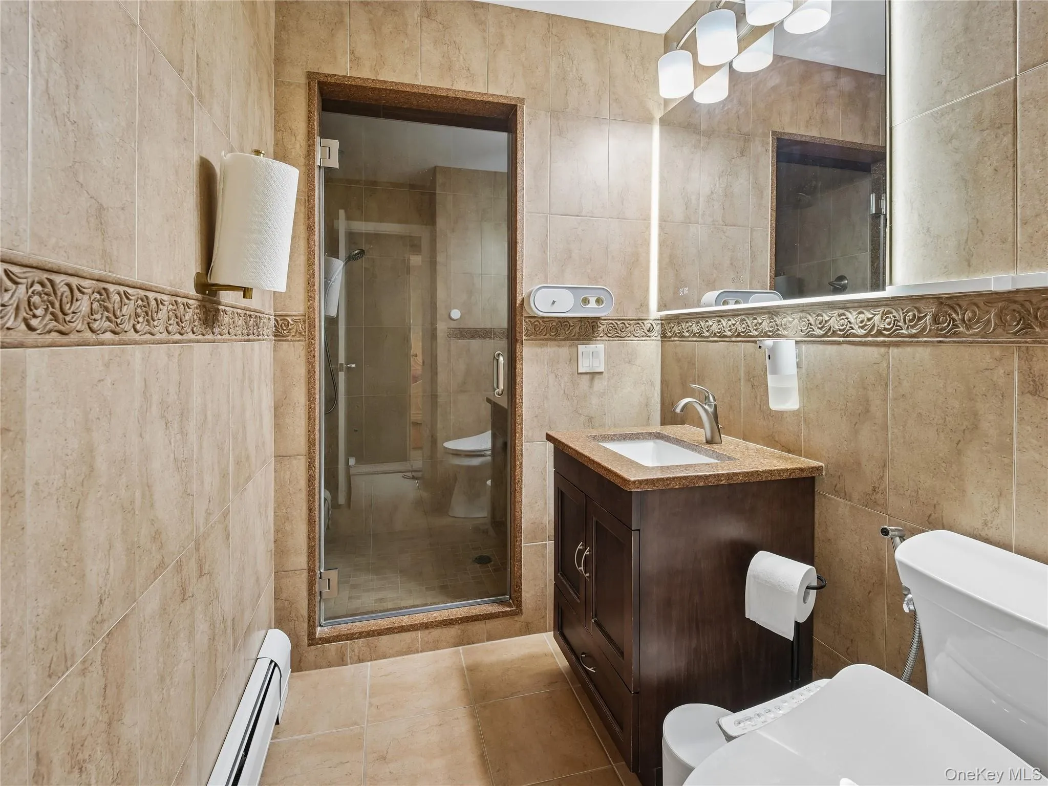Full bathroom featuring ceramic tile walls with glass-enclosed shower, dark wood vanity with counter. Full bathroom featuring ceramic tile walls with glass-enclosed shower, dark wood vanity with counter.
