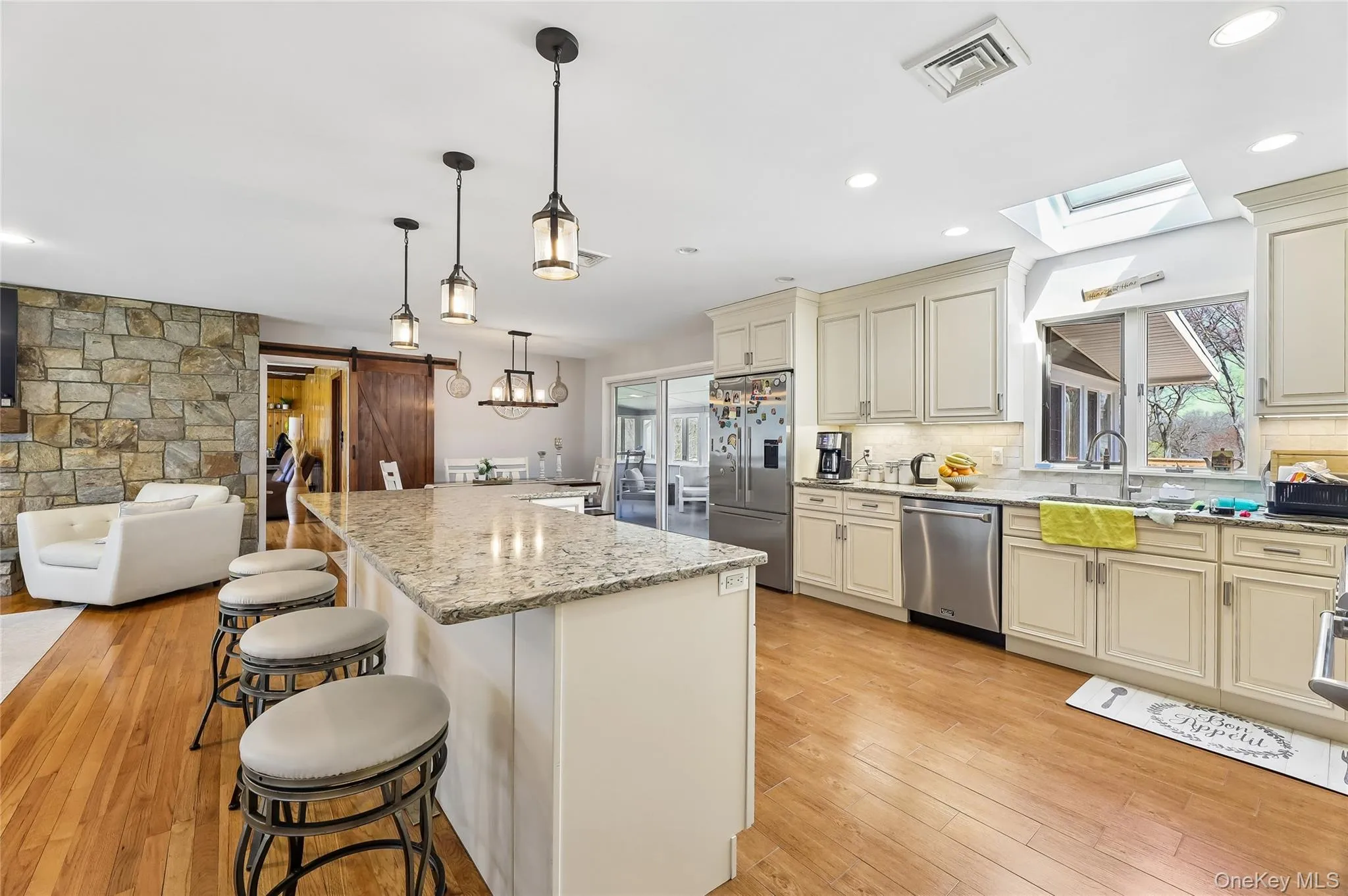 Kitchen featuring a large island with granite-finish countertop, recessed lighting, skylight, stainless steel appliances, and a hardwood-finish flooring Kitchen featuring a large island with granite-finish countertop, recessed lighting, skylight, stainless steel appliances, and a hardwood-finish flooring