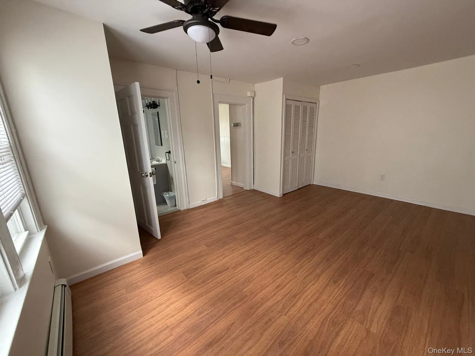 Unfurnished bedroom featuring baseboard heating, wood finished floors, ceiling fan, a closet, and connected bathroom Unfurnished bedroom featuring baseboard heating, wood finished floors, ceiling fan, a closet, and connected bathroom