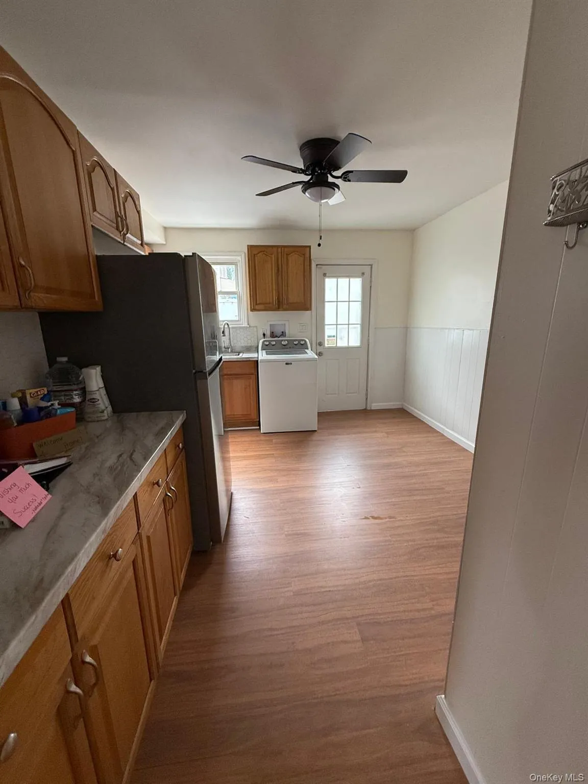 Kitchen featuring wood finish cabinets, wainscoting, freestanding refrigerator, washer / clothes dryer, and light wood-style floors Kitchen featuring wood finish cabinets, wainscoting, freestanding refrigerator, washer / clothes dryer, and light wood-style floors