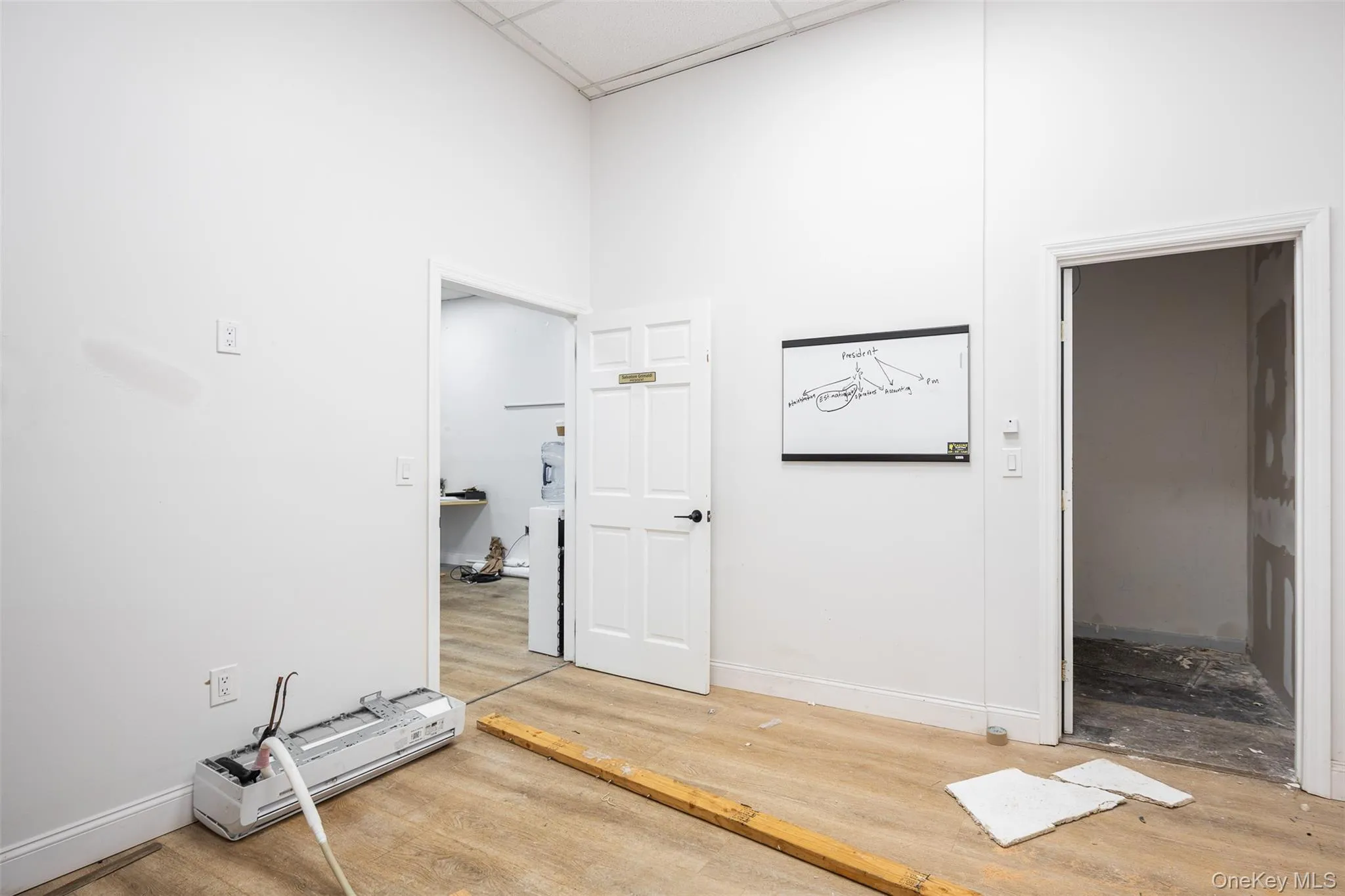 Back office with a drop ceiling, a mini split for heating / cooling, and wood finished floors Back office with a drop ceiling, a mini split for heating / cooling, and wood finished floors