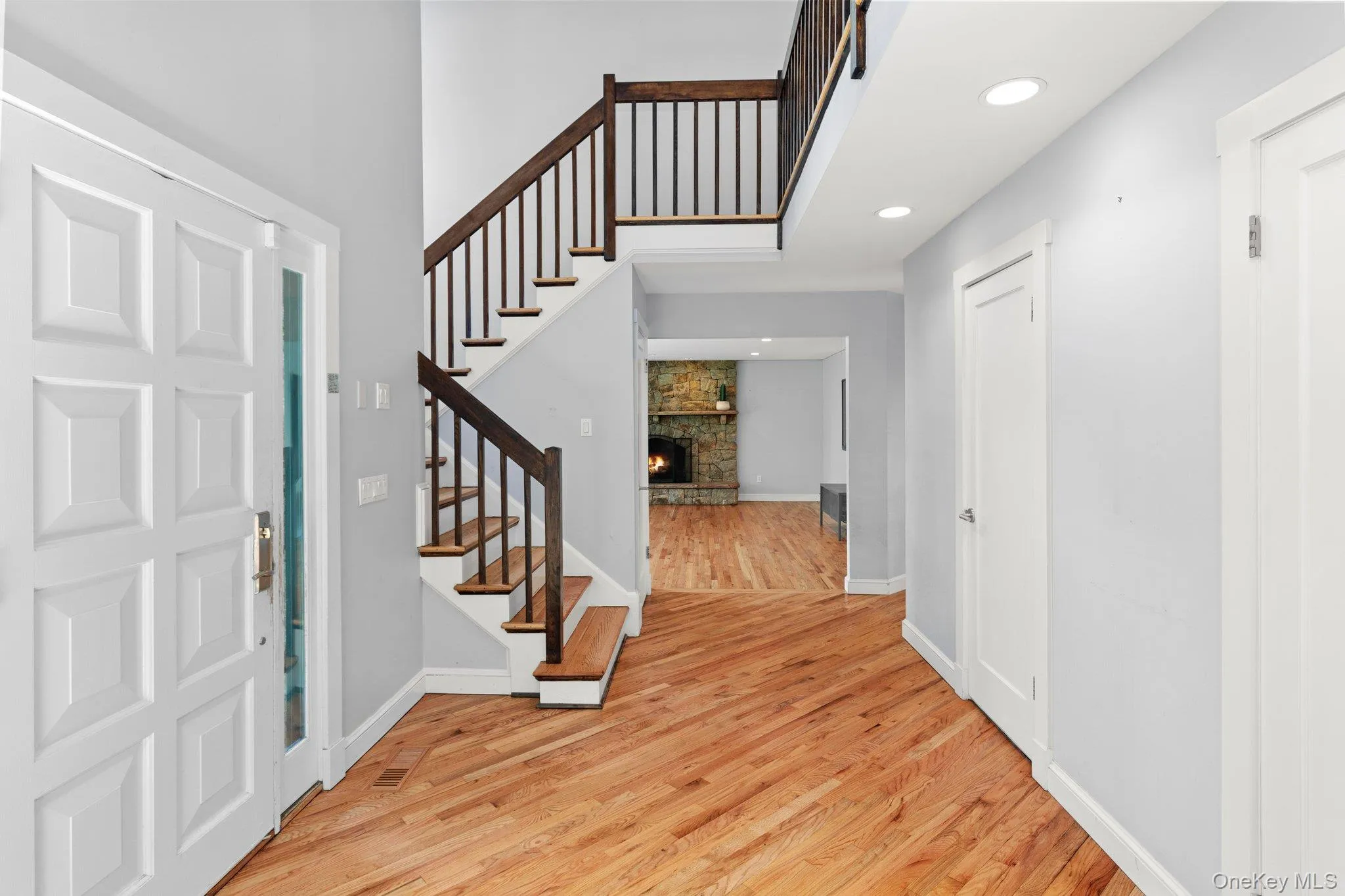 Entrance foyer with light wood-style flooring, baseboards, recessed lighting, stairway, and a stone fireplace Entrance foyer with light wood-style flooring, baseboards, recessed lighting, stairway, and a stone fireplace