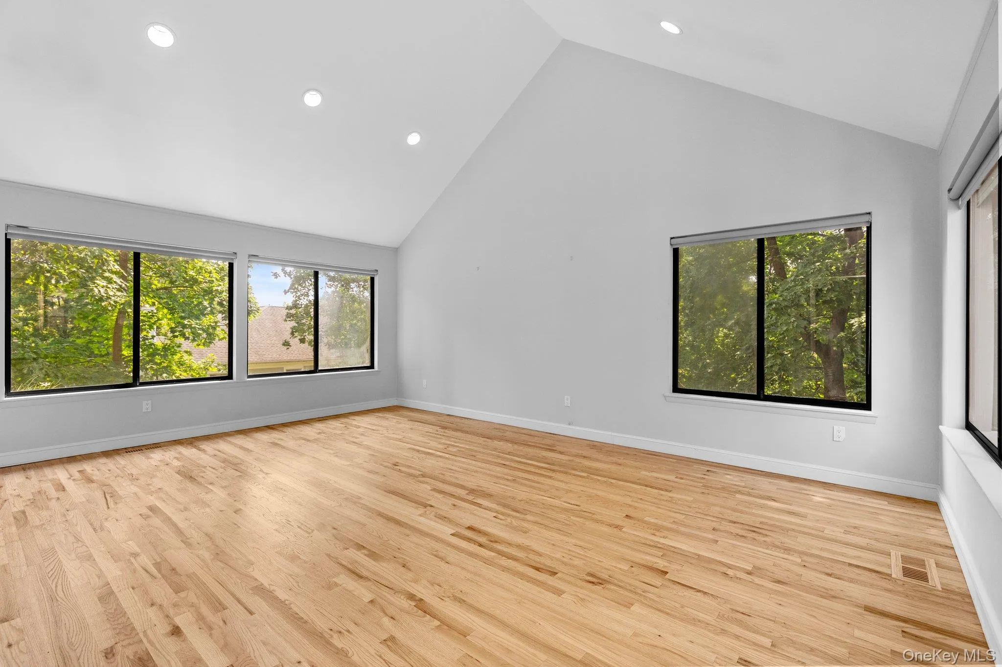 Empty room featuring high vaulted ceiling, wood finished floors, baseboards, visible vents, and recessed lighting Empty room featuring high vaulted ceiling, wood finished floors, baseboards, visible vents, and recessed lighting