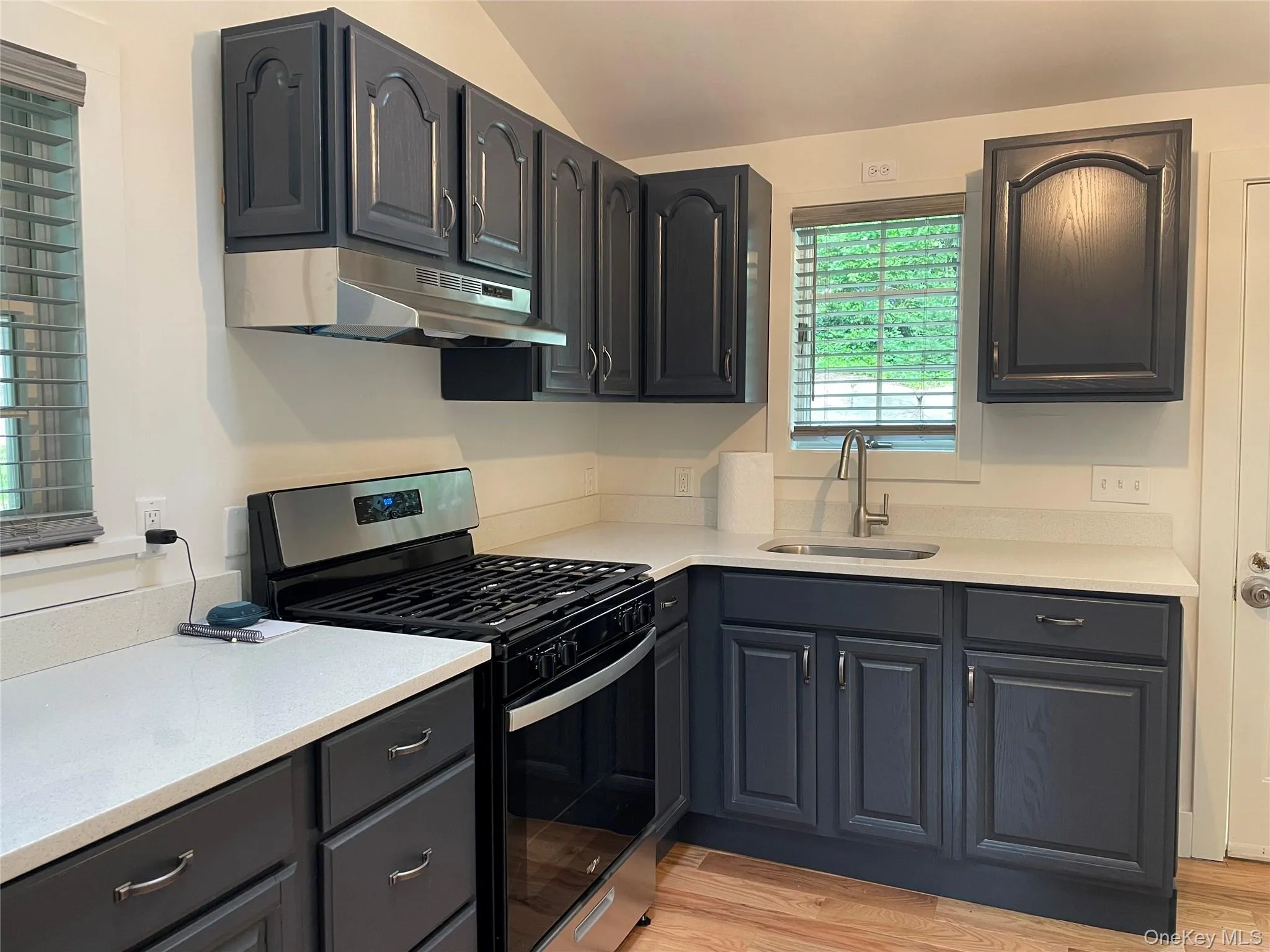 Kitchen featuring gas range, a sink, under cabinet range hood, vaulted ceiling, and light countertops Kitchen featuring gas range, a sink, under cabinet range hood, vaulted ceiling, and light countertops