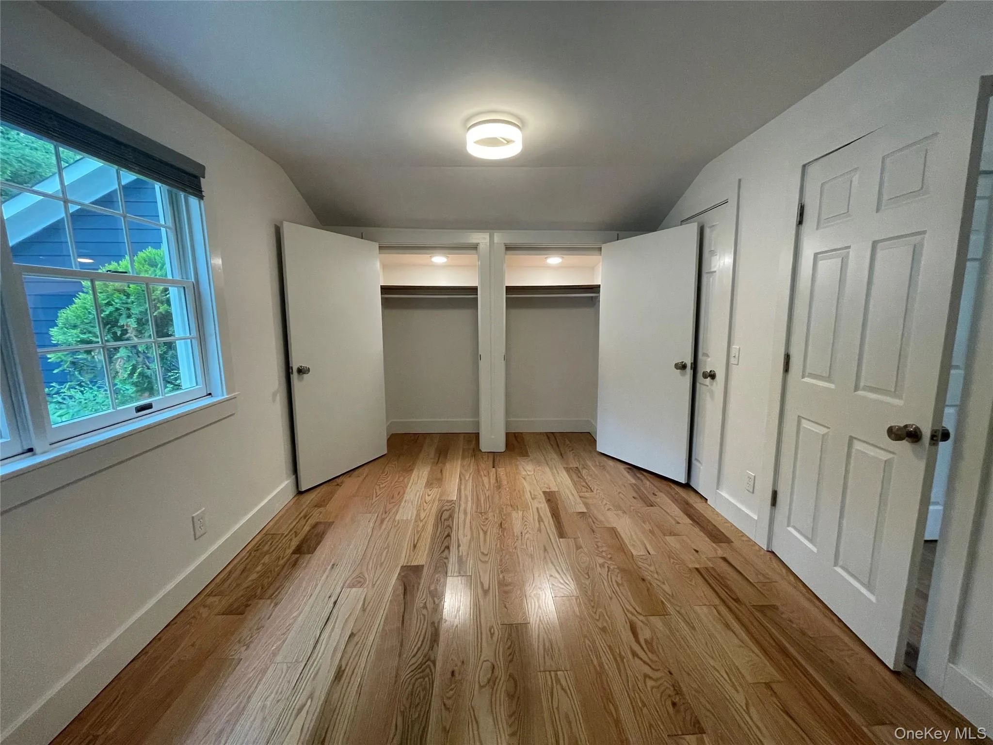 Unfurnished bedroom with vaulted ceiling, multiple closets, light wood-style floors, and baseboards Unfurnished bedroom with vaulted ceiling, multiple closets, light wood-style floors, and baseboards