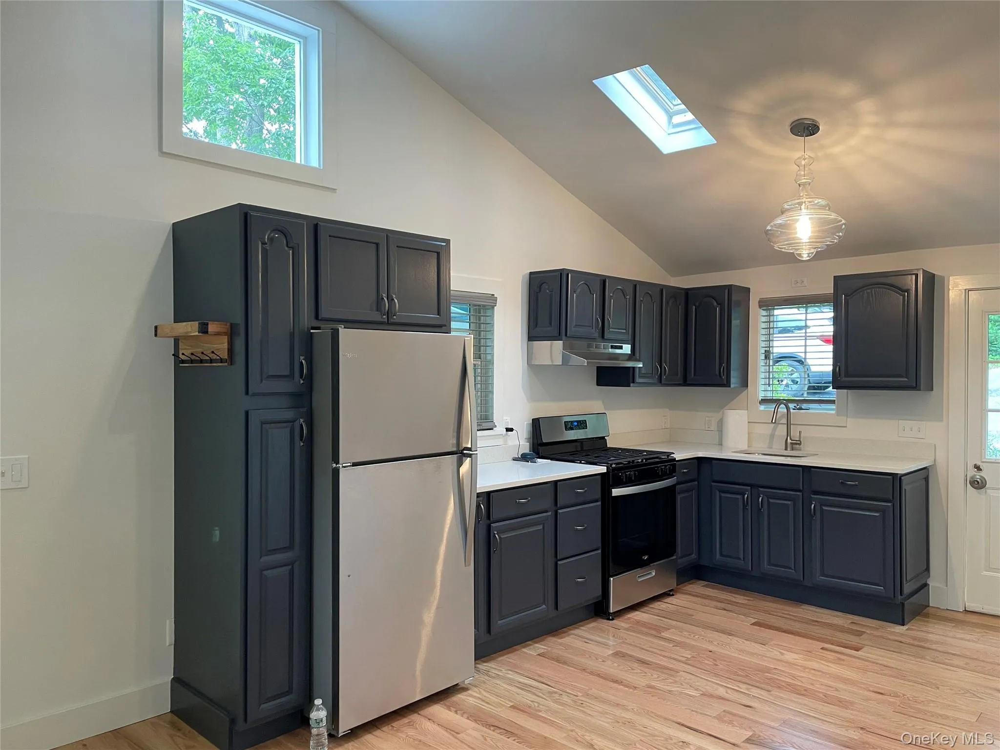 Kitchen featuring appliances with stainless steel finishes, a sink, a skylight, under cabinet range hood, and light countertops Kitchen featuring appliances with stainless steel finishes, a sink, a skylight, under cabinet range hood, and light countertops