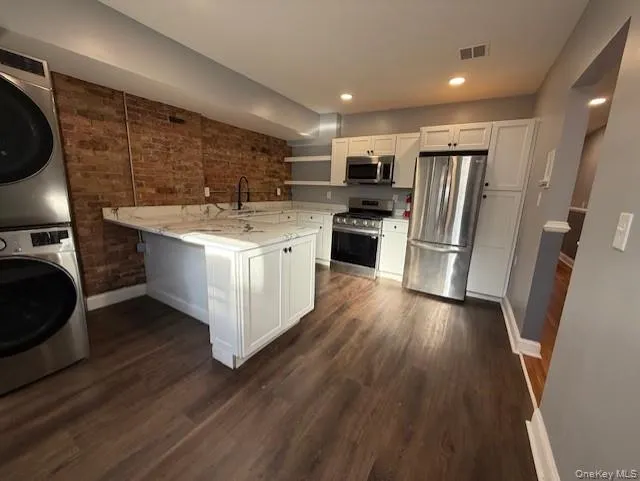 Kitchen with brick wall, white cabinets, stainless steel appliances, open shelves, and dark wood-type flooring Kitchen with brick wall, white cabinets, stainless steel appliances, open shelves, and dark wood-type flooring