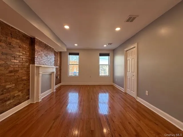 Unfurnished living room featuring brick wall, hardwood / wood-style flooring, a fireplace, and recessed lighting Unfurnished living room featuring brick wall, hardwood / wood-style flooring, a fireplace, and recessed lighting