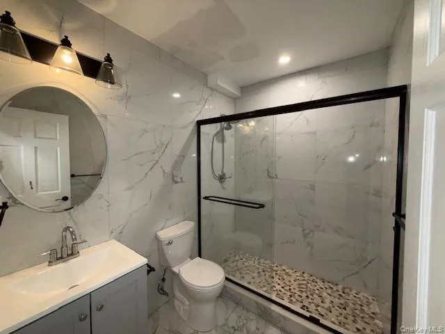 Bathroom featuring tile walls, vanity, marble tiled flooring, a marble finish shower, and stone wall Bathroom featuring tile walls, vanity, marble tiled flooring, a marble finish shower, and stone wall