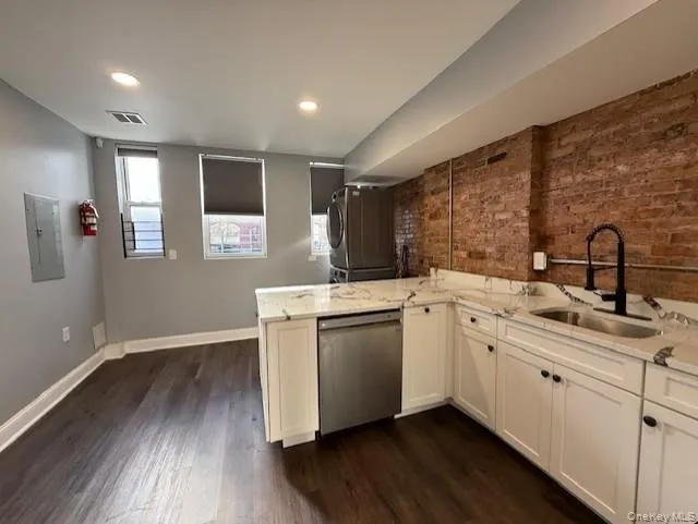Kitchen with brick wall, light stone counters, white cabinets, dishwasher, and a peninsula Kitchen with brick wall, light stone counters, white cabinets, dishwasher, and a peninsula