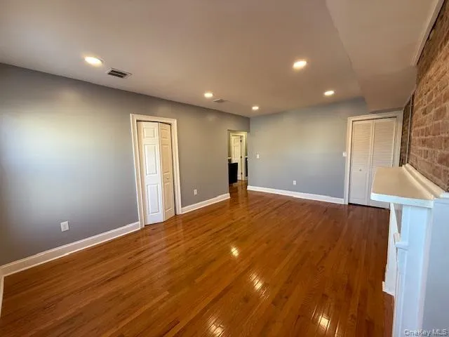 Unfurnished living room featuring hardwood / wood-style flooring, recessed lighting, and brick wall Unfurnished living room featuring hardwood / wood-style flooring, recessed lighting, and brick wall