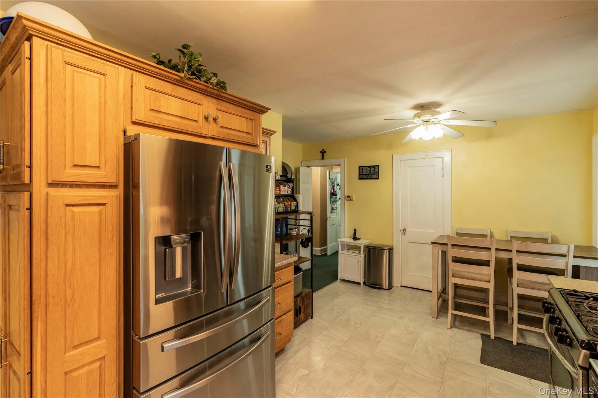 Kitchen featuring extensive wood cabinetry, stainless steel refrigerator, tile flooring, ceiling fan, and a dining area with a high-top table and chairs Kitchen featuring extensive wood cabinetry, stainless steel refrigerator, tile flooring, ceiling fan, and a dining area with a high-top table and chairs