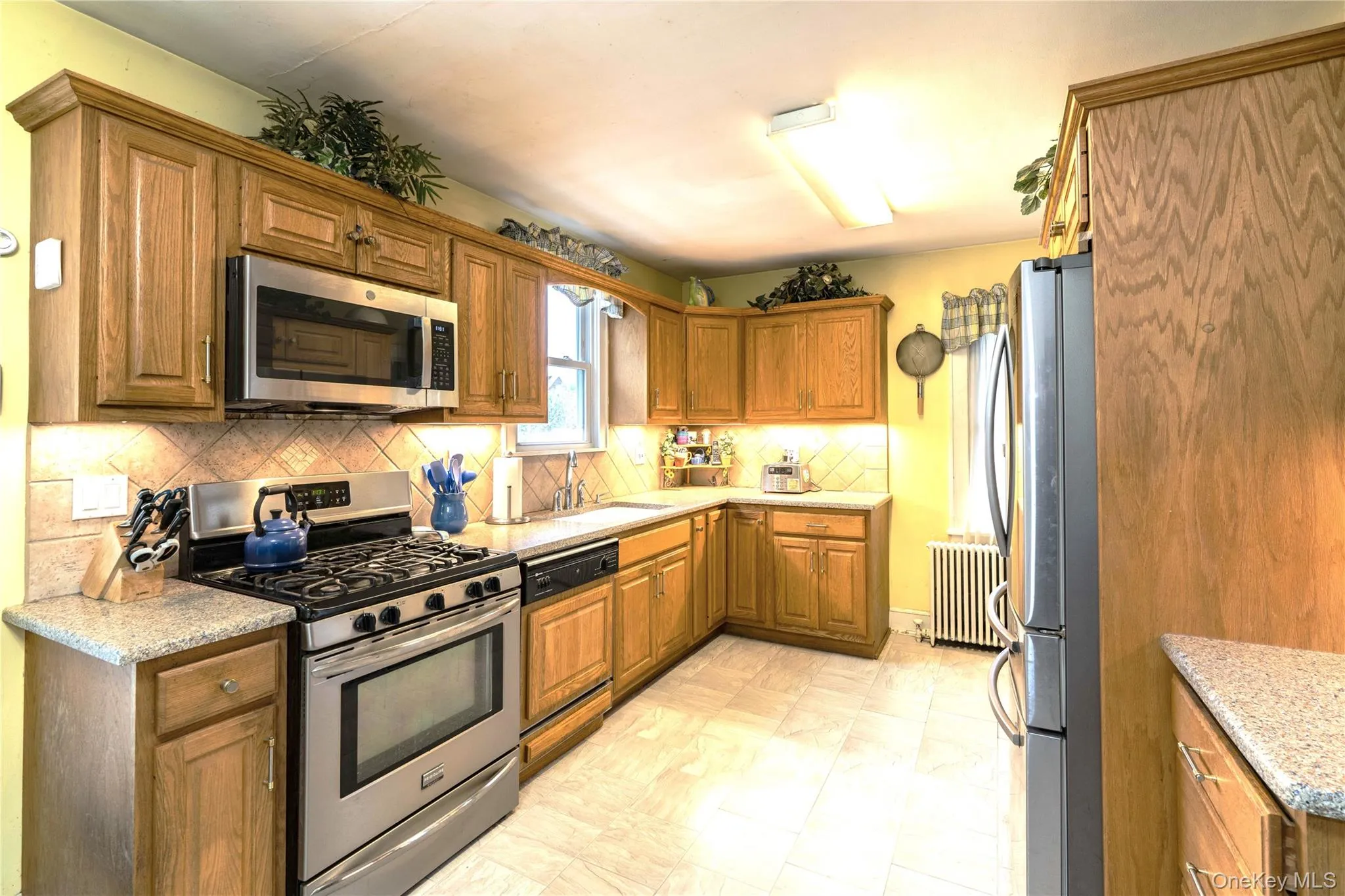 Kitchen featuring wood cabinetry, stainless steel appliances, speckled countertops, a tile backsplash,, Kitchen featuring wood cabinetry, stainless steel appliances, speckled countertops, a tile backsplash,,